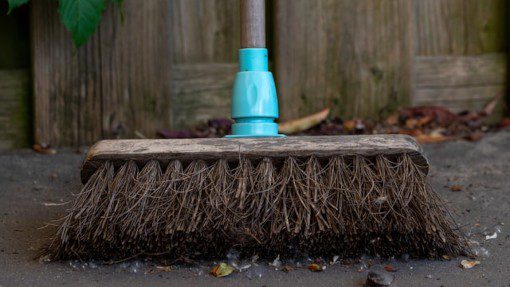 Broom with a blue handle resting against a fence