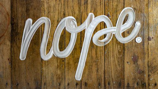 The word nope handwritten in white paint on a wooden floor