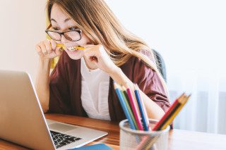 Woman biting a yellow pencil while sitting in front of a laptop